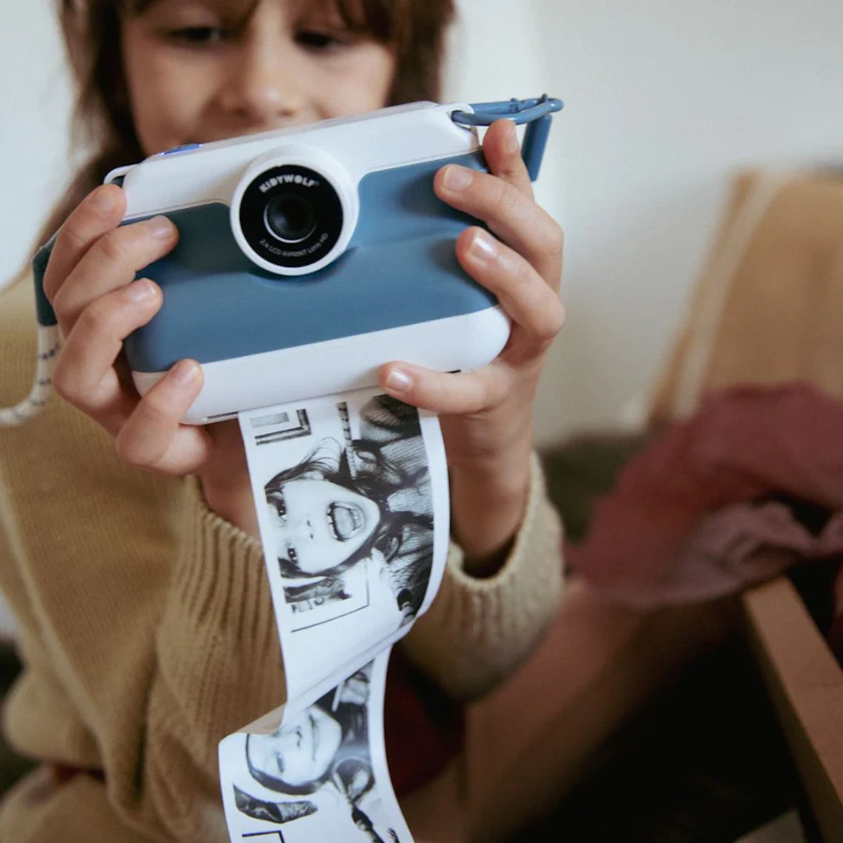 Child using a blue Kidywolf Kidyprint camera to print black and white thermal photos instantly.