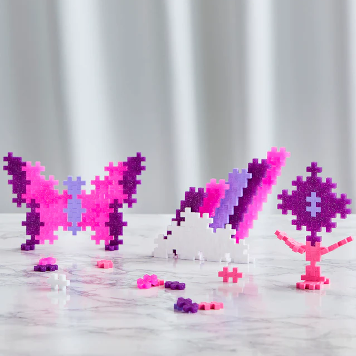 Plus-Plus glitter building blocks used to create a butterfly, cloud, and flower in pink, purple, and white.