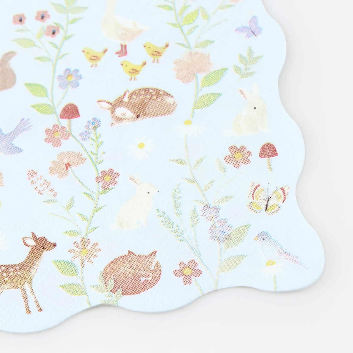 Light blue scalloped napkin with pastel illustrations of woodland animals, birds, flowers, and mushrooms.
