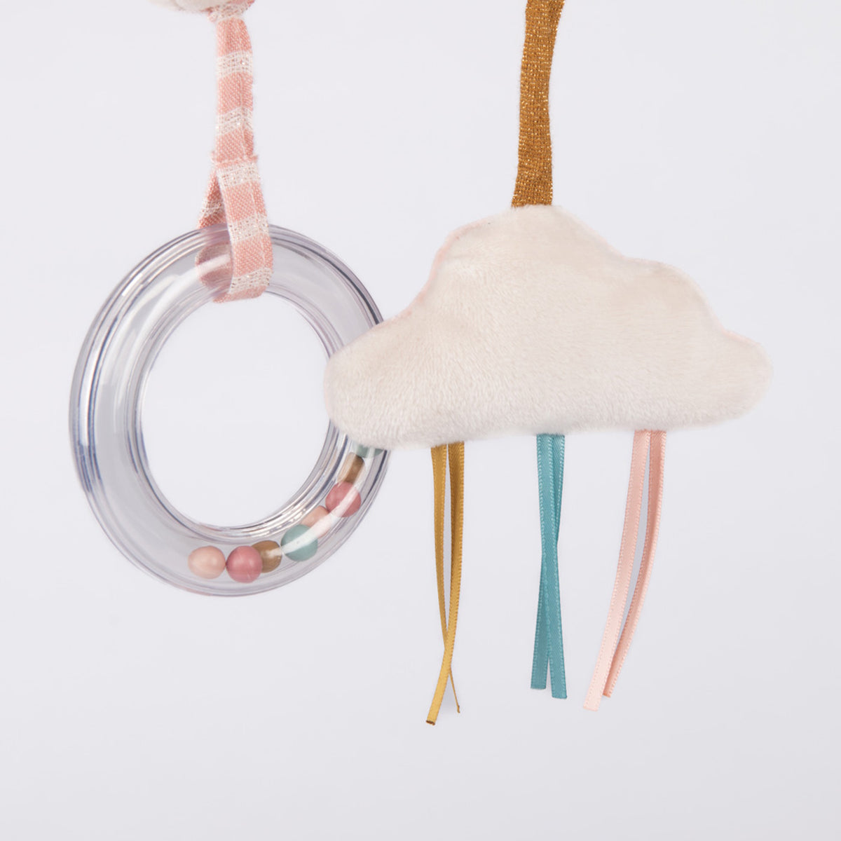 A baby rattle with colorful beads inside a clear ring hanging next to a plush white cloud with dangling ribbons.