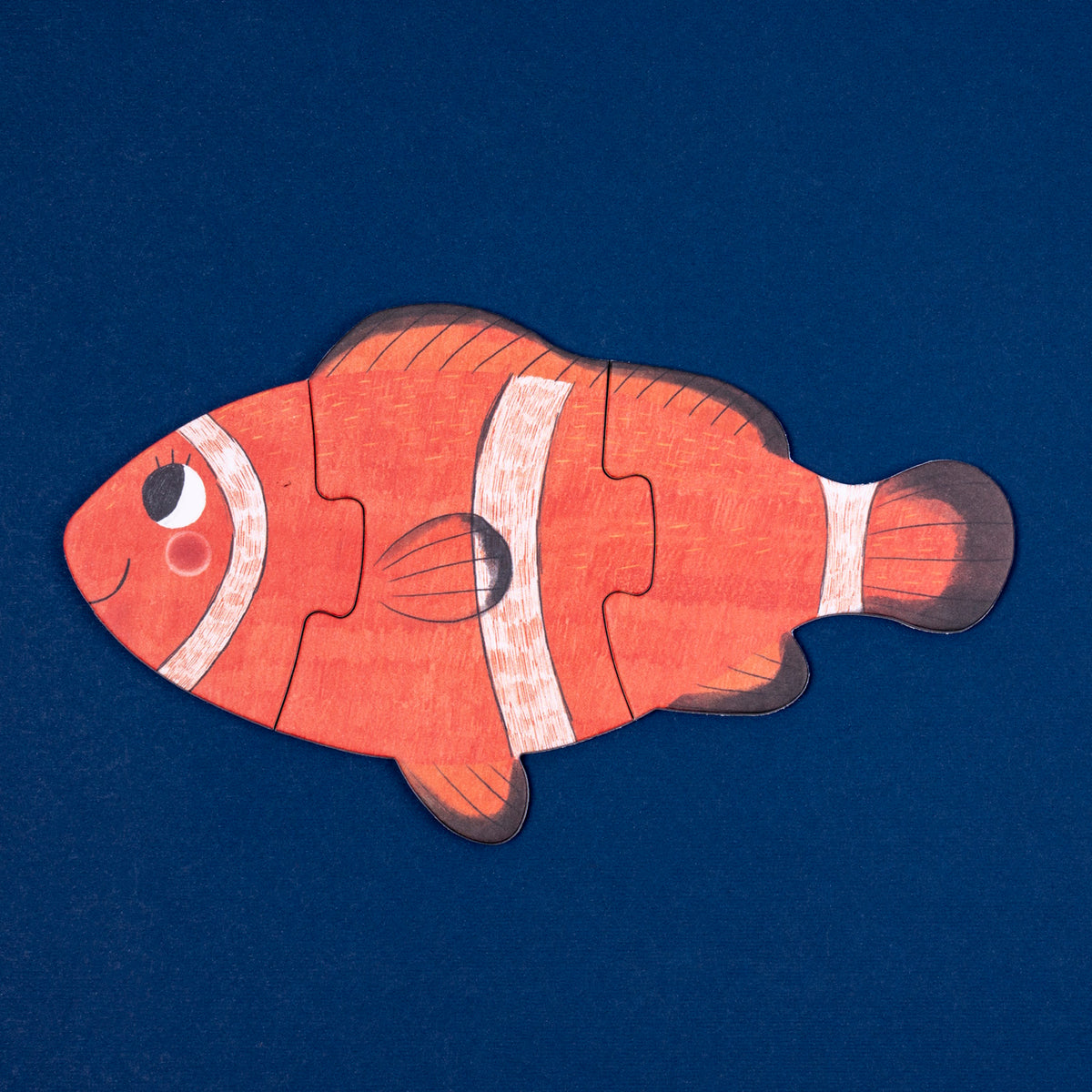 Orange and white Londji clownfish wooden jigsaw puzzle for kids on a textured dark blue background.