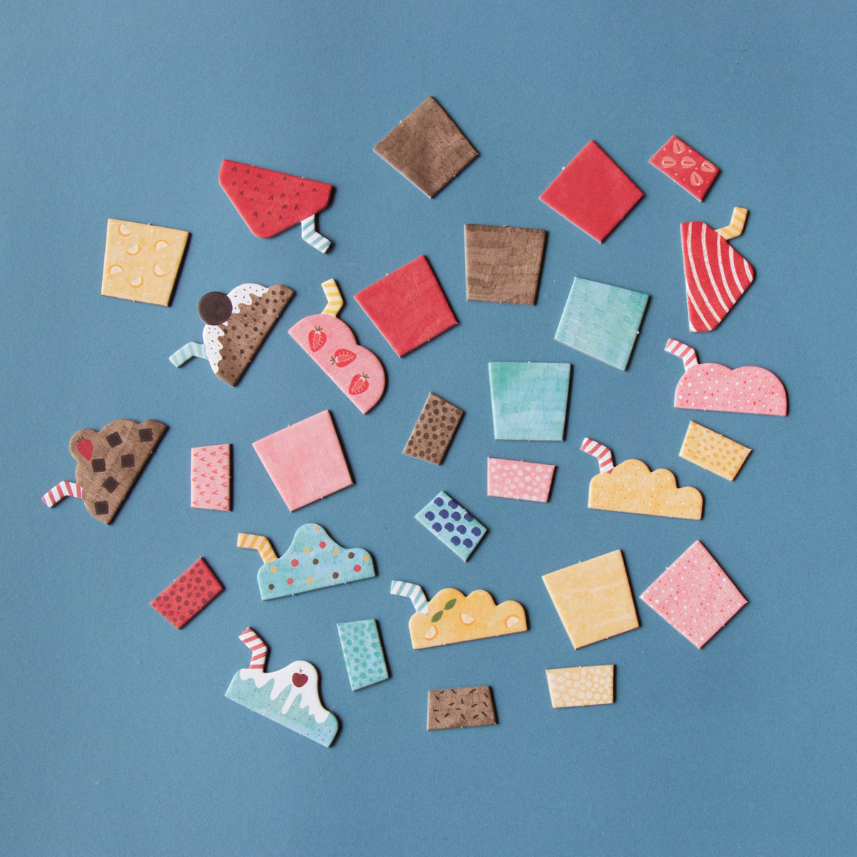 Colorful toy milkshake and sundae pieces with patterns and straws scattered on a flat blue background.