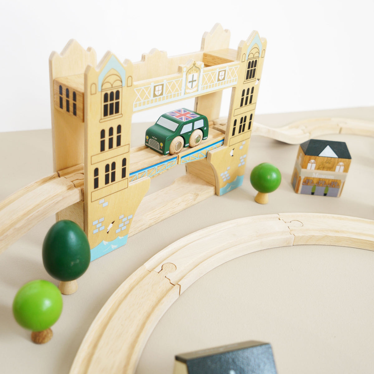 Wooden toy car crossing a Tower Bridge track piece with mini trees and buildings.