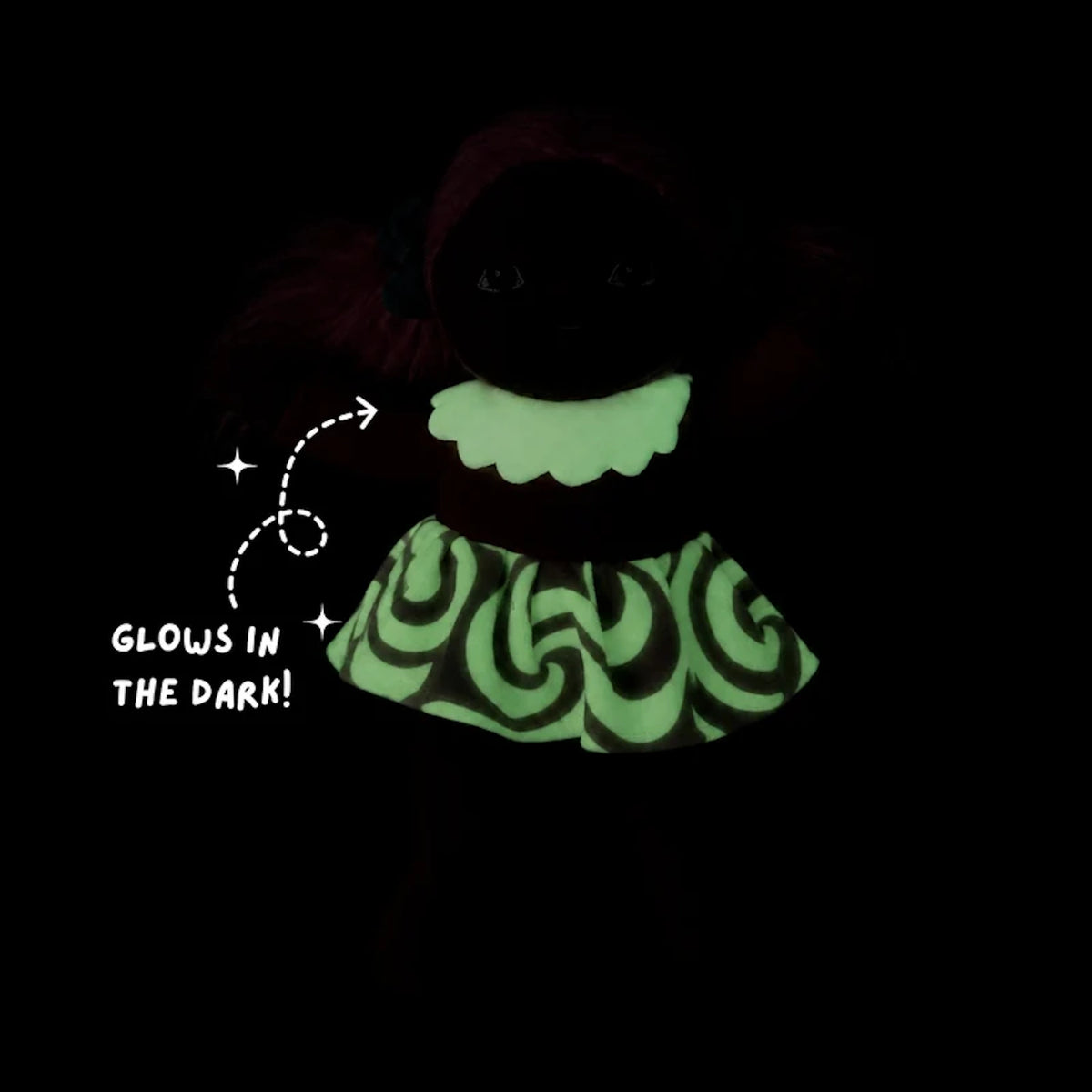 Plush doll in a dark setting with glowing green collar and swirl skirt patterns.