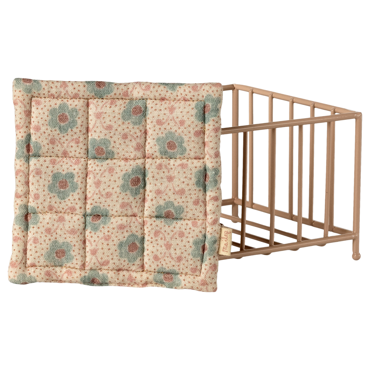 Vintage-style beige and blue floral quilted pillow leaning against a small, light brown wooden crib on a white background. The scene feels nostalgic and cozy.