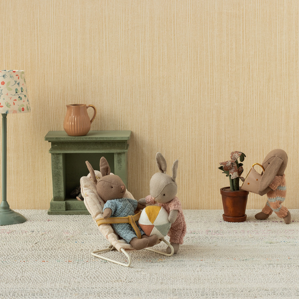 Maileg micro rabbits playing in a dollhouse room with a bouncer, ball, and watering can.