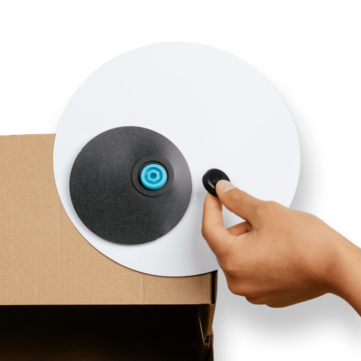Hand attaching a large googly eye prop onto a cardboard box using a blue plastic connector.