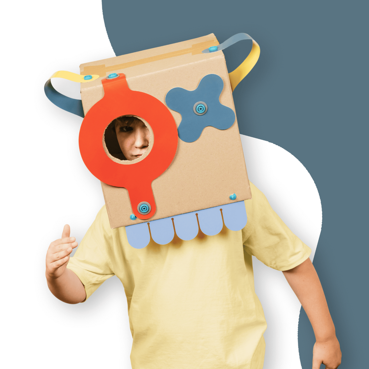 Child wearing a decorated cardboard box monster mask with colorful craft shapes attached.