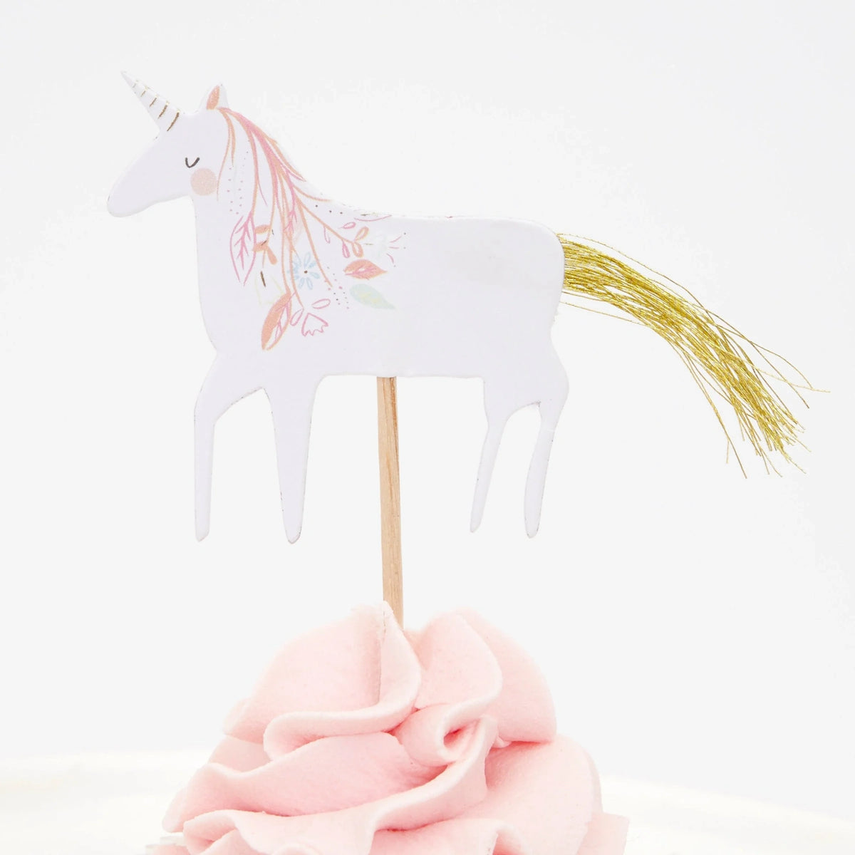 A white unicorn cupcake topper with a gold tinsel tail and pink mane details, set in pink frosting.