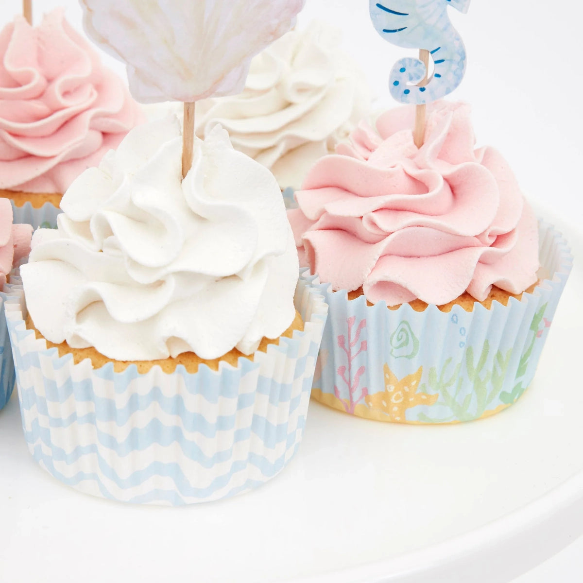 Pink and white cupcakes with under-the-sea themed liners and decorative toppers.