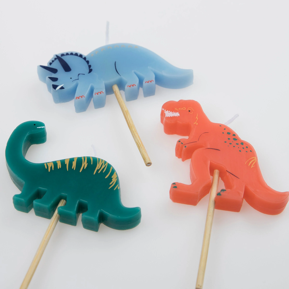 Close-up view of three dinosaur-shaped birthday candles featuring a Triceratops, Brachiosaurus, and T-Rex.