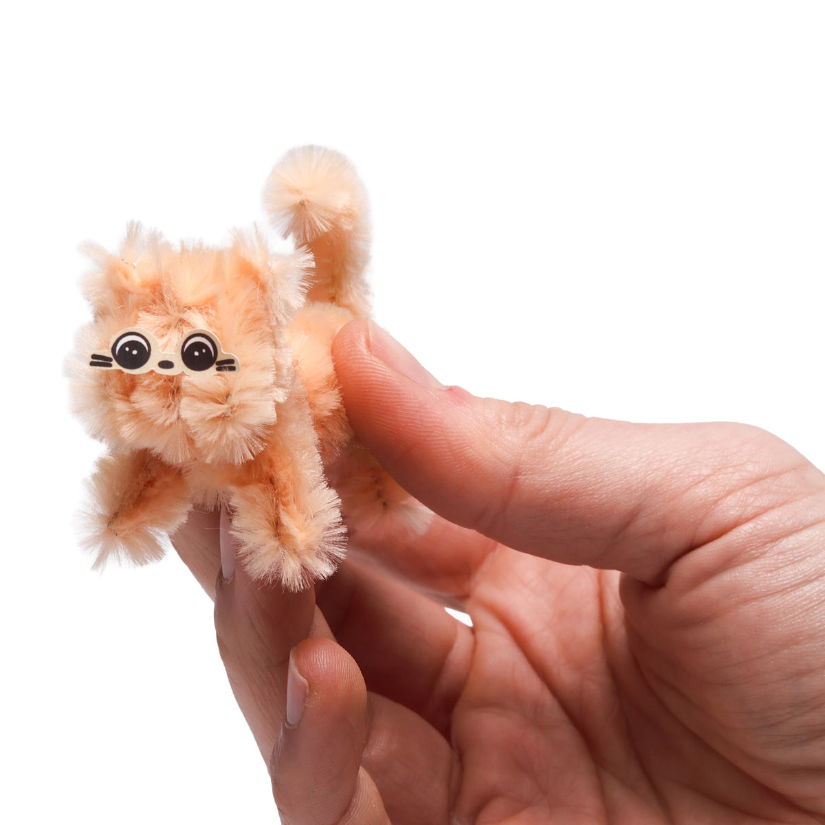 Hand holding a tiny, fluffy orange cat craft made from pipe cleaners with a cute face sticker.