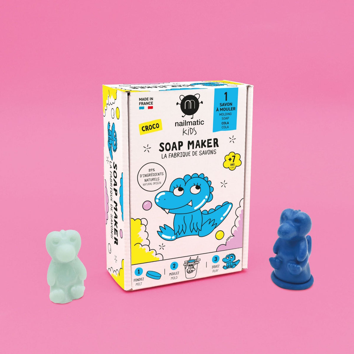 A colorful soap-making kit labeled "Nailmatic Kids" on a pink background. Features cartoon crocodile art and two soaps, one blue, one pale green. Fun and playful.