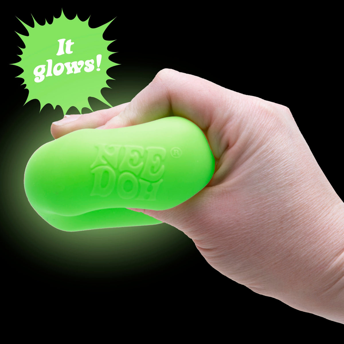 Hand squishing a glowing green NeeDoh sensory toy on a black background with "It glows!" text.