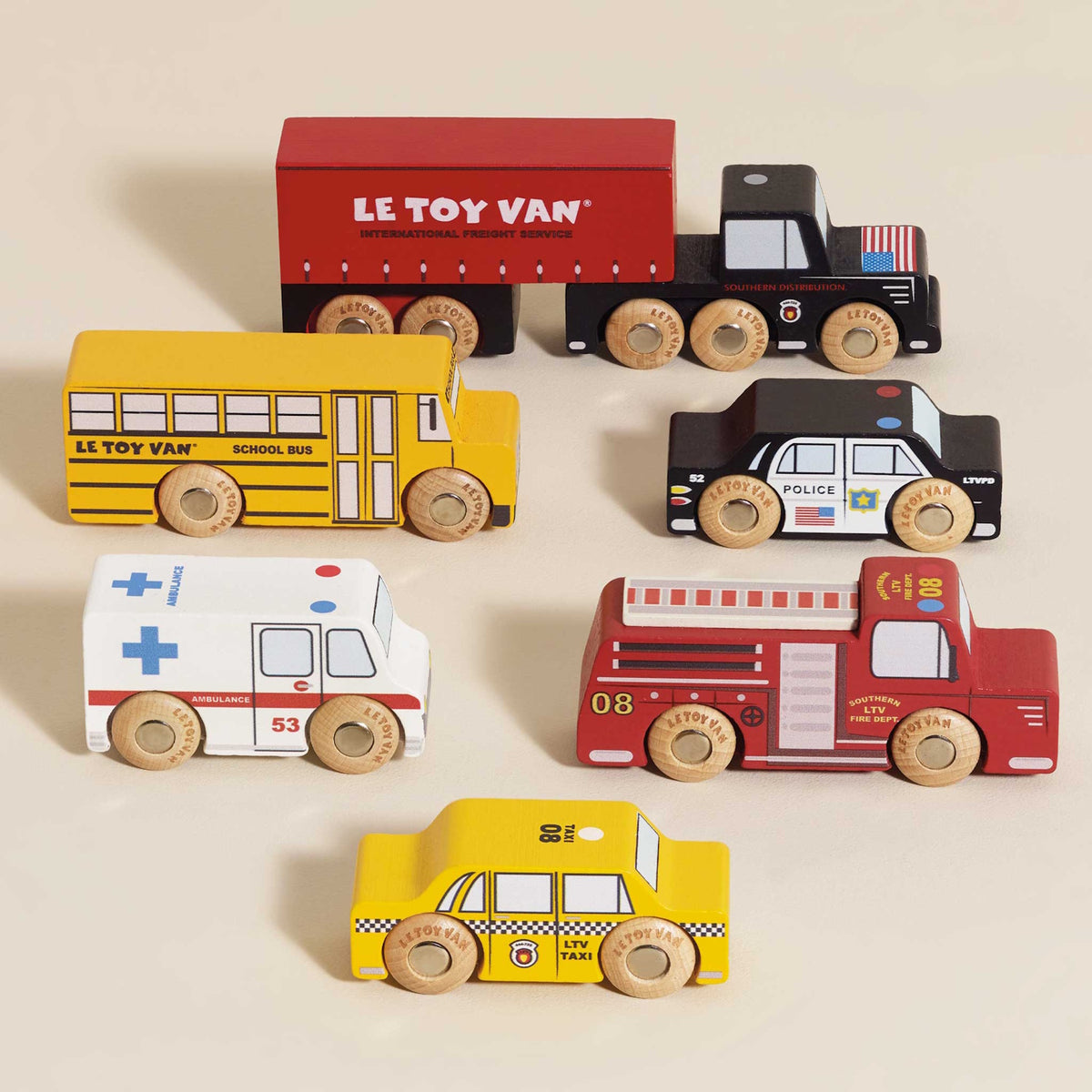 Set of six wooden toy city vehicles neatly arranged on a neutral beige background.