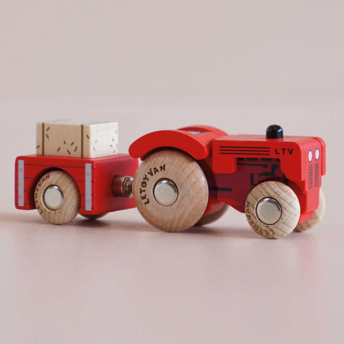 Red wooden toy tractor with a matching trailer carrying a hay bale, shown in a side view.