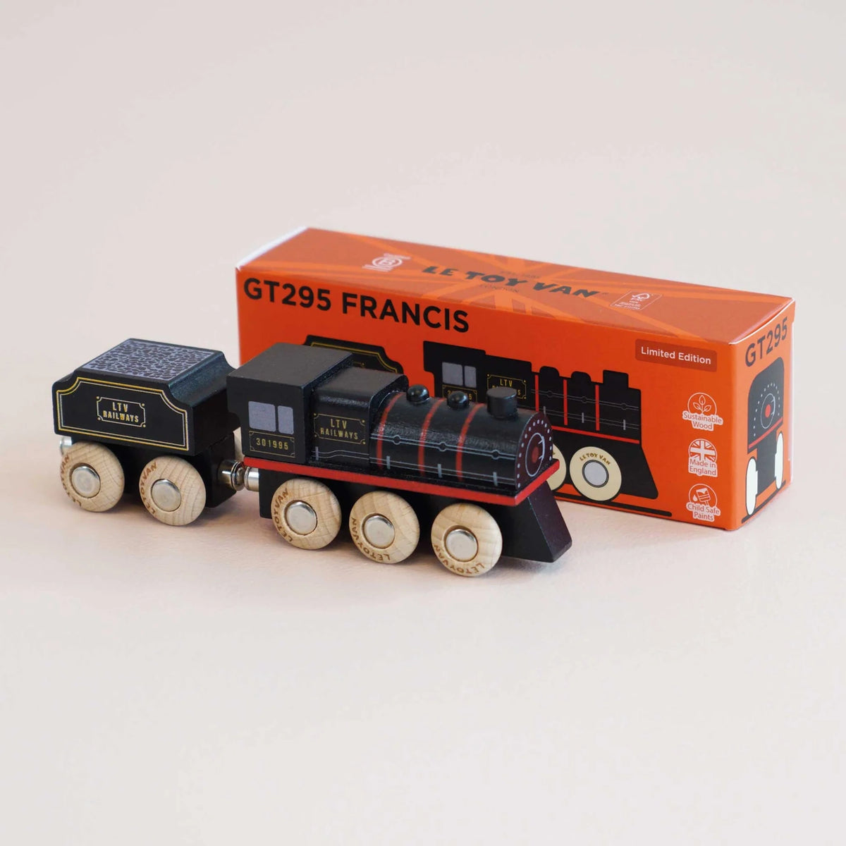 Black wooden toy steam train with natural wheels parked beside its orange packaging box labeled GT295 FRANCIS.