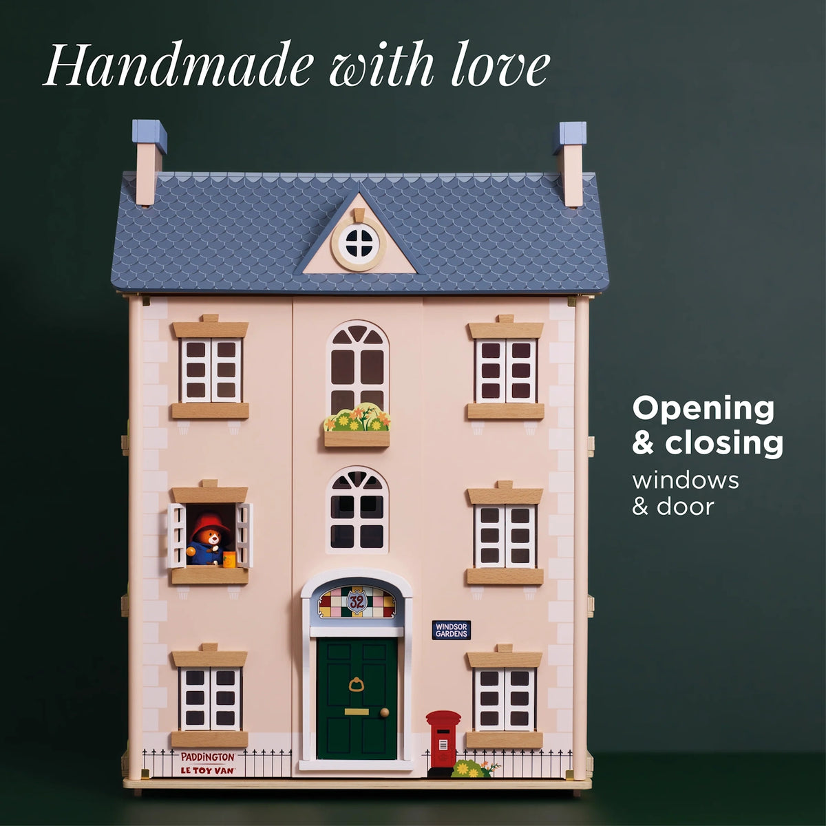 Wooden dollhouse featuring a blue roof, green front door, and Paddington looking out an open window.