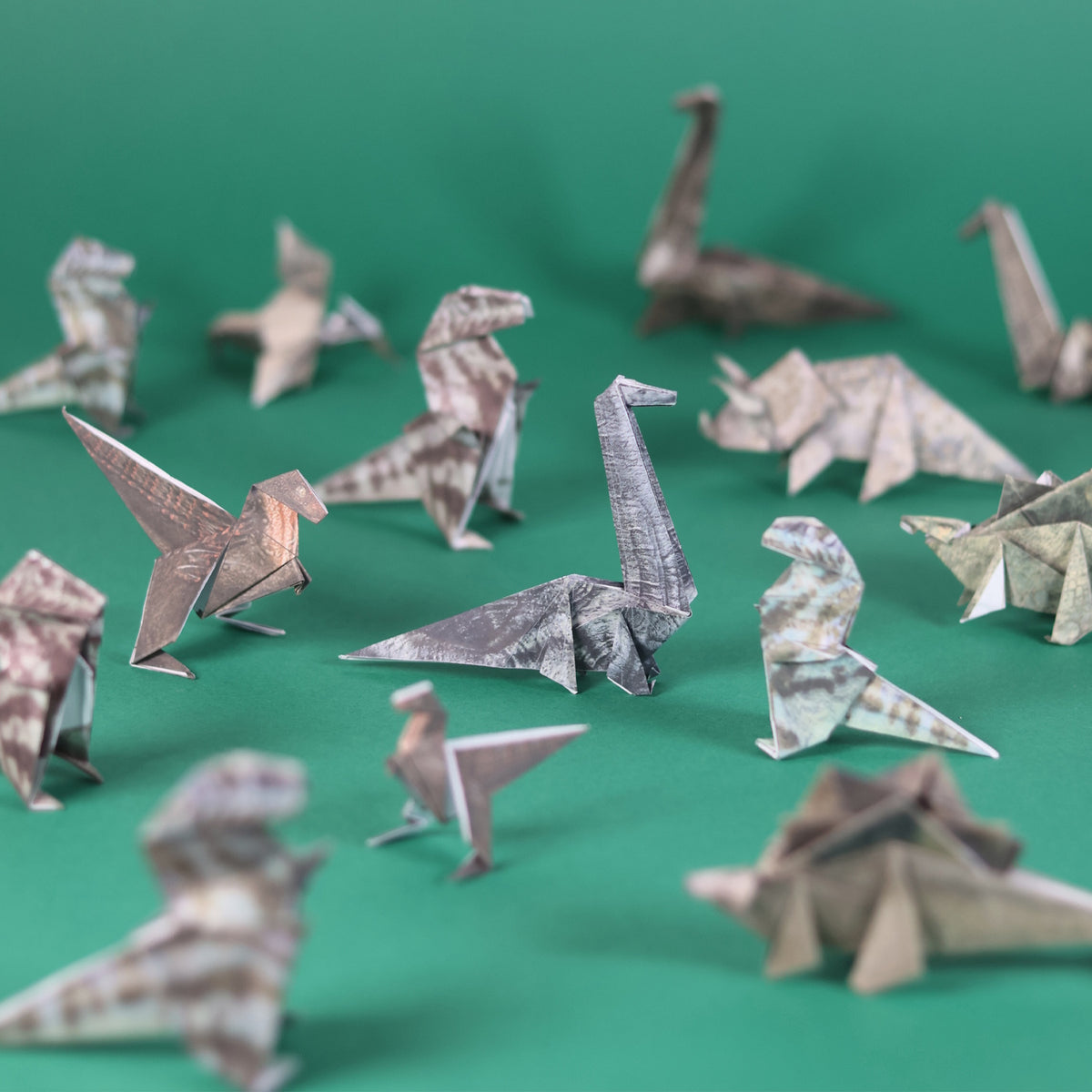 A variety of patterned origami paper dinosaurs arranged across a plain green surface.