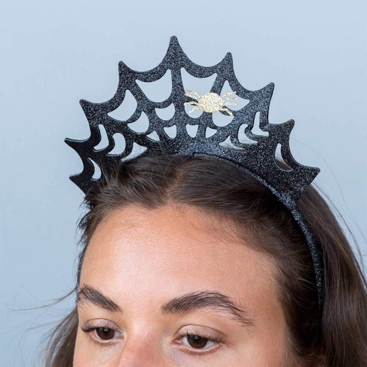 Close-up of a woman wearing a black glitter spiderweb headband with a small gold spider.