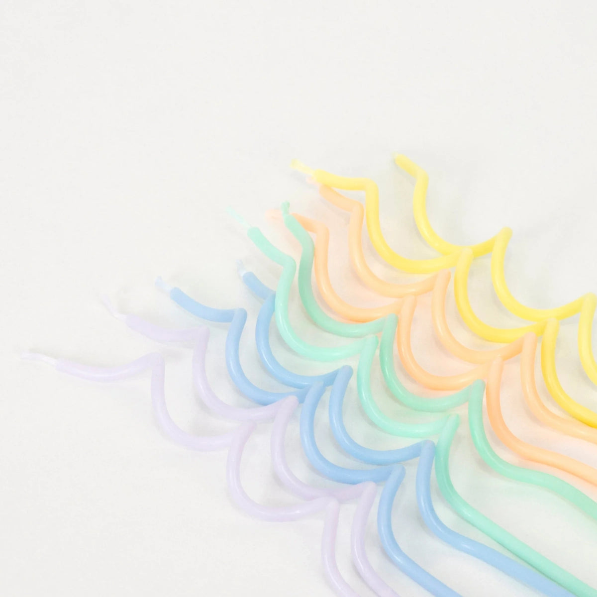 An assortment of colorful, pastel-toned swirly candles in shades of yellow, orange, green, blue, and purple on white background.