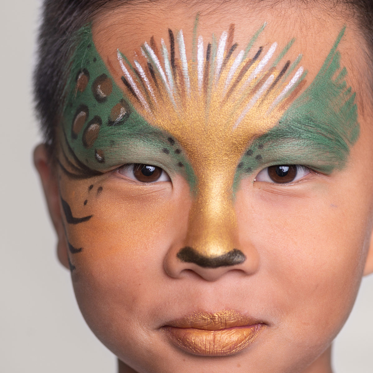 A close-up of a child with an animal-inspired face paint design in gold, green, and brown tones, resembling a jungle creature.