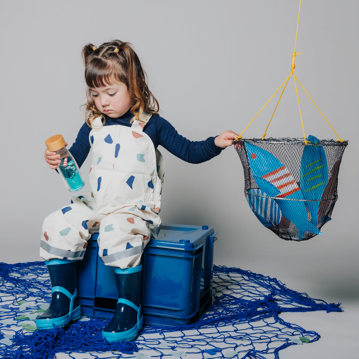 Girl holding a sensory bottle while reaching for a hanging net filled with toys.