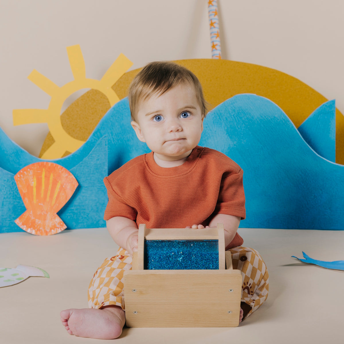 Baby sitting on the floor and looking forward while holding a wooden sensory roller.