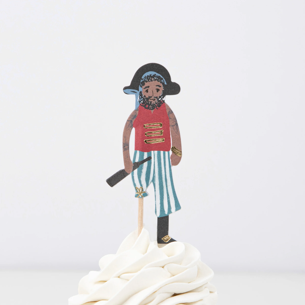 Pirate crew member topper in a red shirt and striped pants on a wooden pick in swirled white frosting.