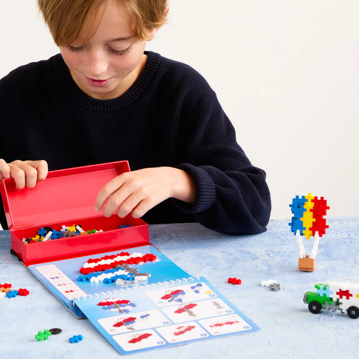 Child using a Plus-Plus activity pad to build a colorful hot air balloon and truck with interlocking puzzle blocks.