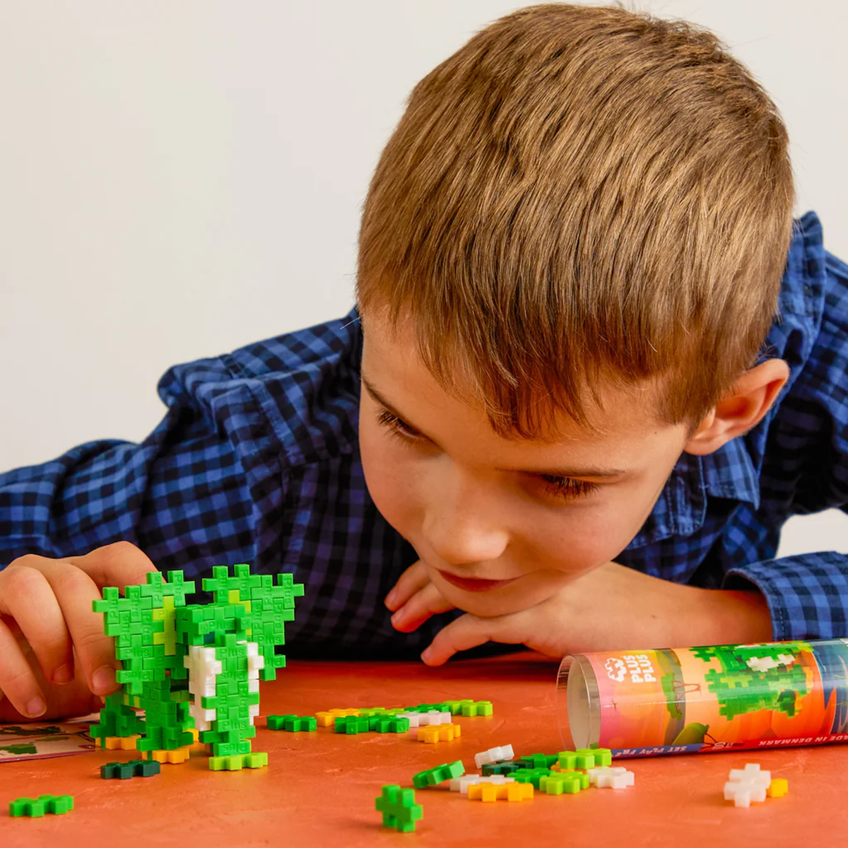 Young boy building a green elephant with Plus-Plus construction blocks on an orange surface.