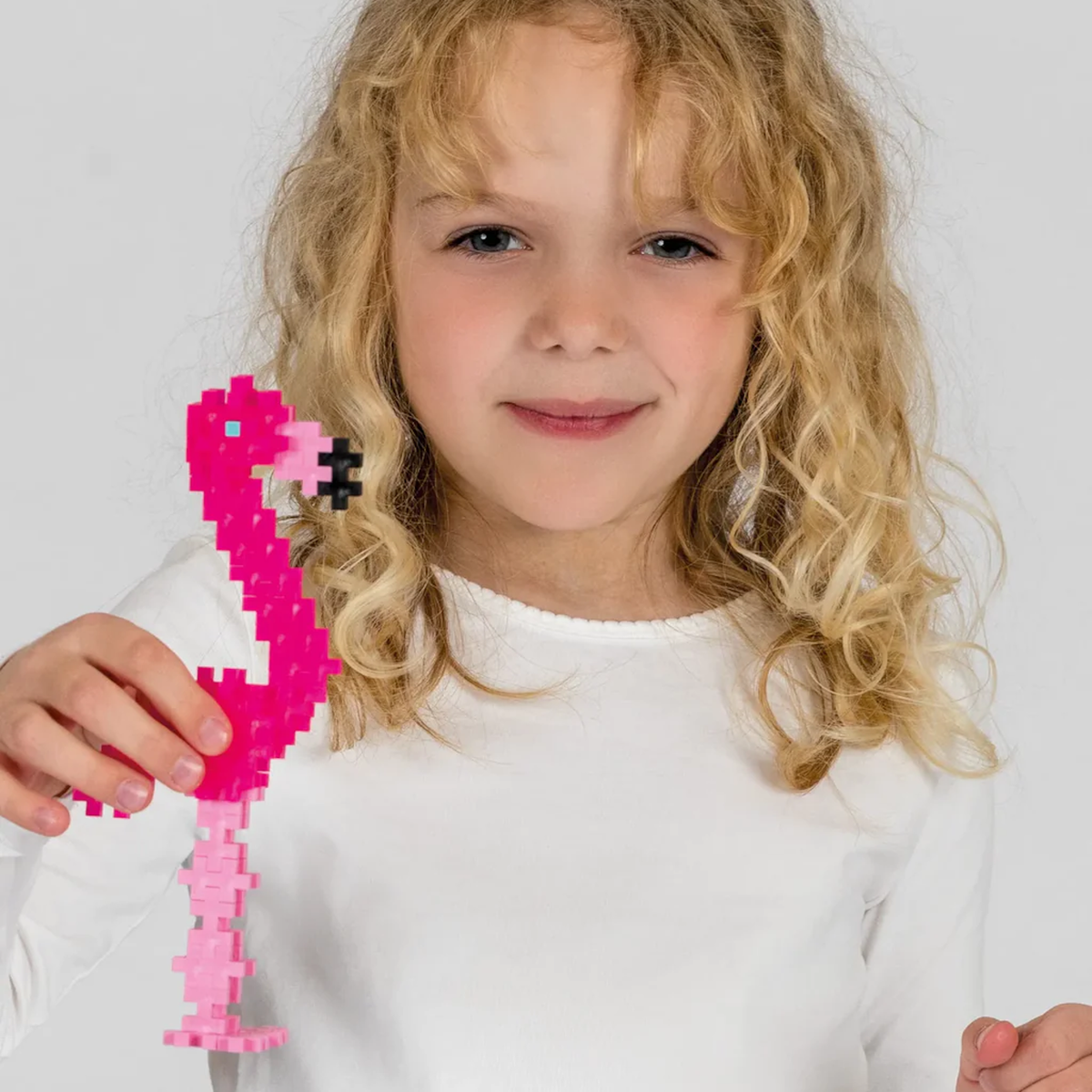 Young girl holding a pink flamingo made of Plus-Plus building blocks.