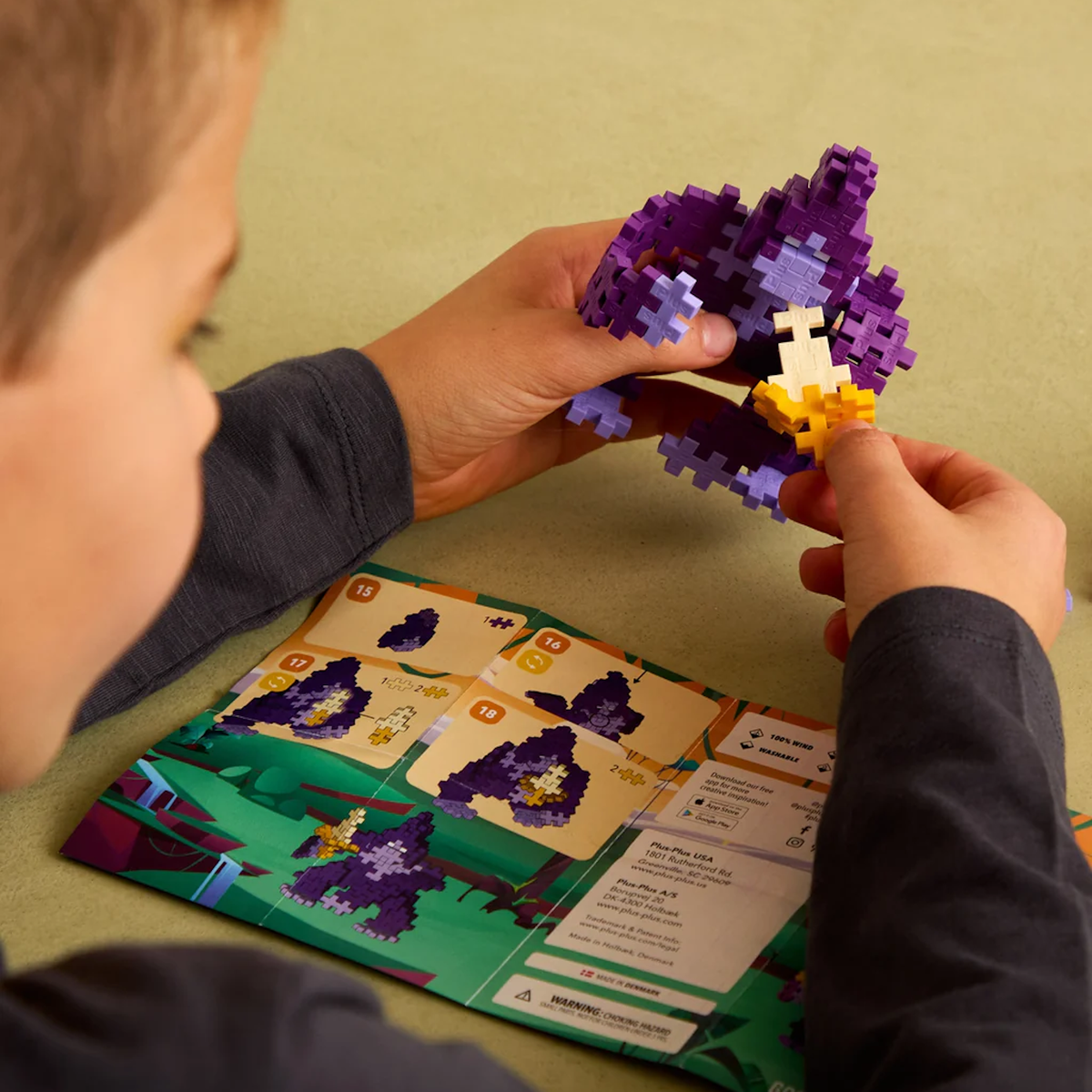 Child building a purple gorilla with Plus-Plus blocks, following an instruction manual. Simple, creative STEM toy play.