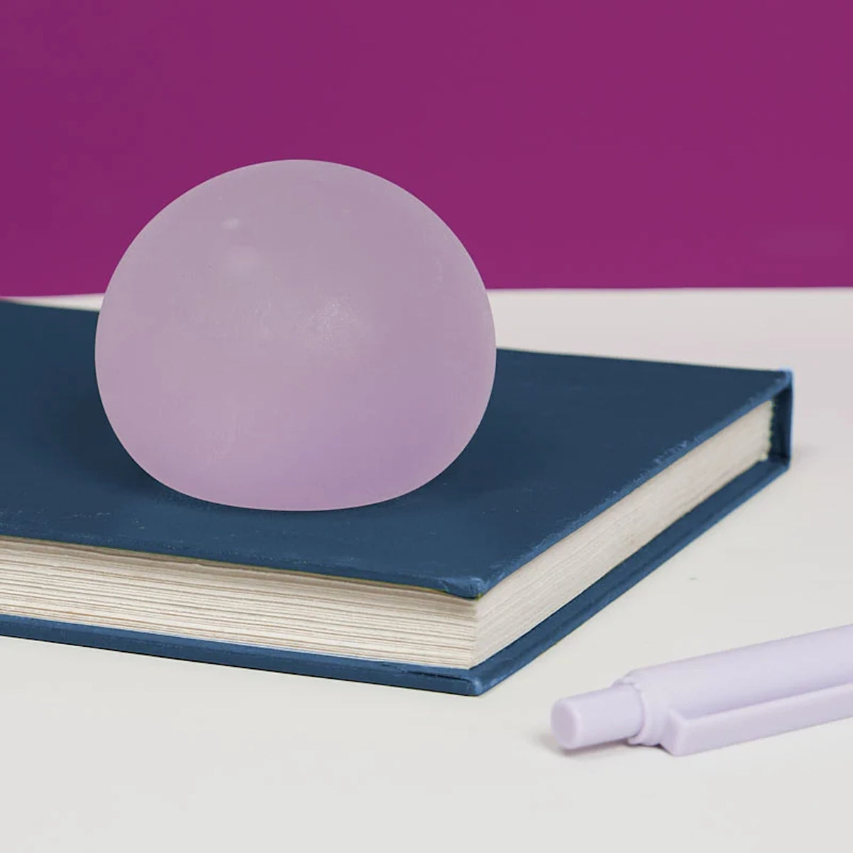 A purple translucent Speks stress ball resting on a closed blue notebook next to a lavender pen.