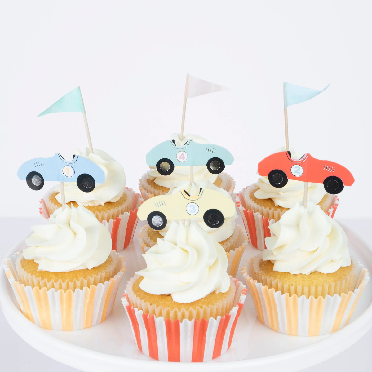 Group of cupcakes with striped liners, swirled frosting, and vintage race car and flag toppers.