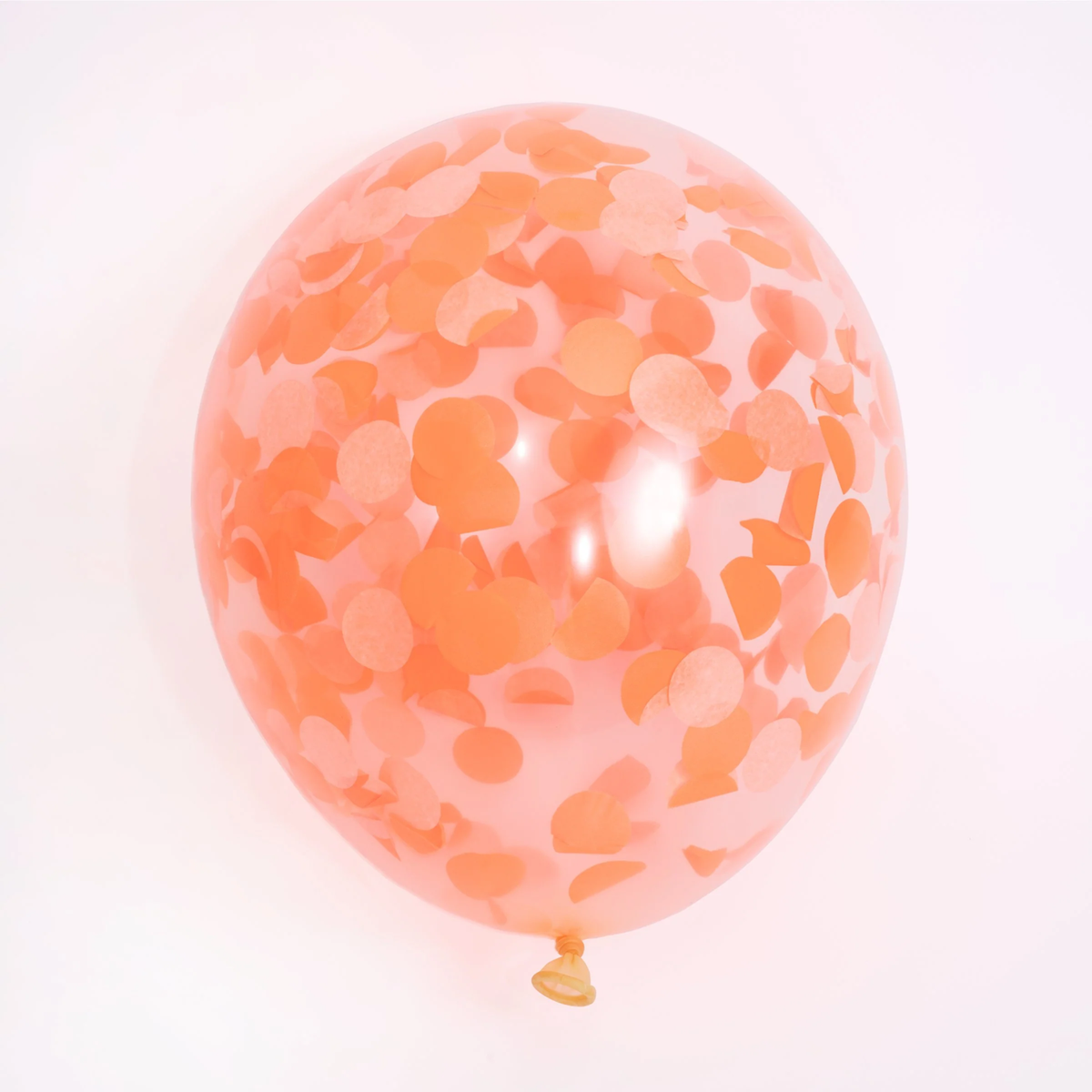 Single inflated clear party balloon filled with orange round tissue paper confetti against a white background.