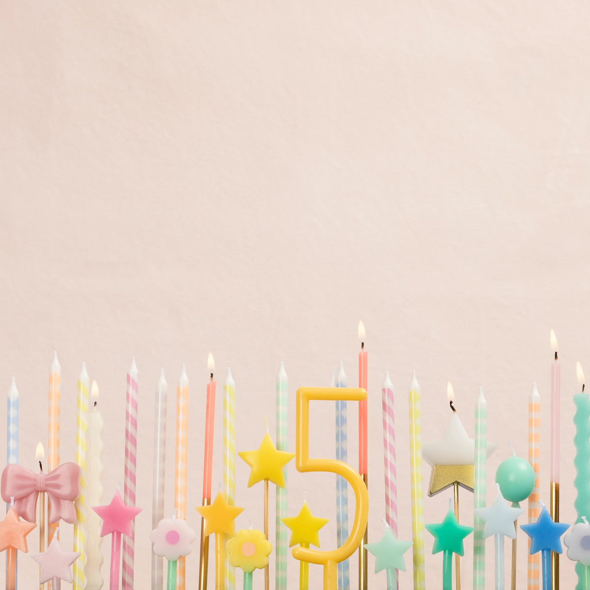 An array of lit pastel birthday candles, including stars, bows, and a number five candle.