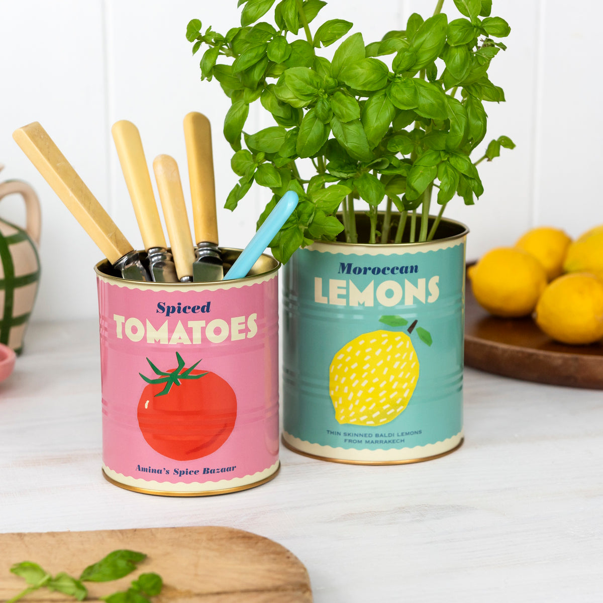 Vintage cans repurposed as containers; one with utensils has a "Spiced Tomatoes" label, and the other holds basil, labeled "Moroccan Lemons." Lemons in the background.