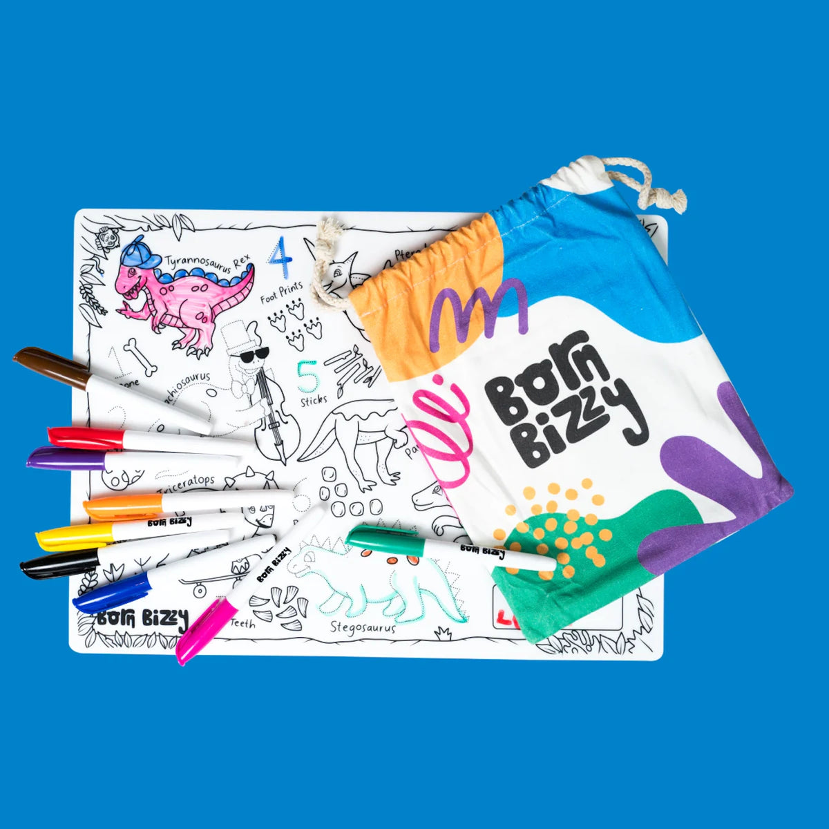 A dinosaur coloring mat with multi-colored markers and a "Born Bizzy" drawstring storage bag on a blue background.