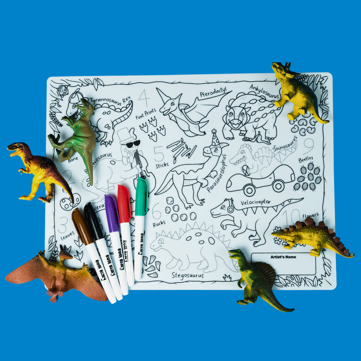 A dinosaur-themed coloring mat with plastic toy dinosaurs, markers, and line drawings of various dinosaurs.