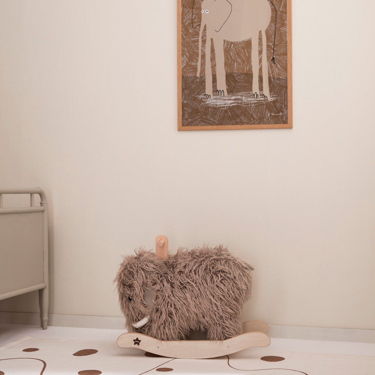 Plush mammoth rocking horse in a nursery room with an elephant framed picture on the wall.