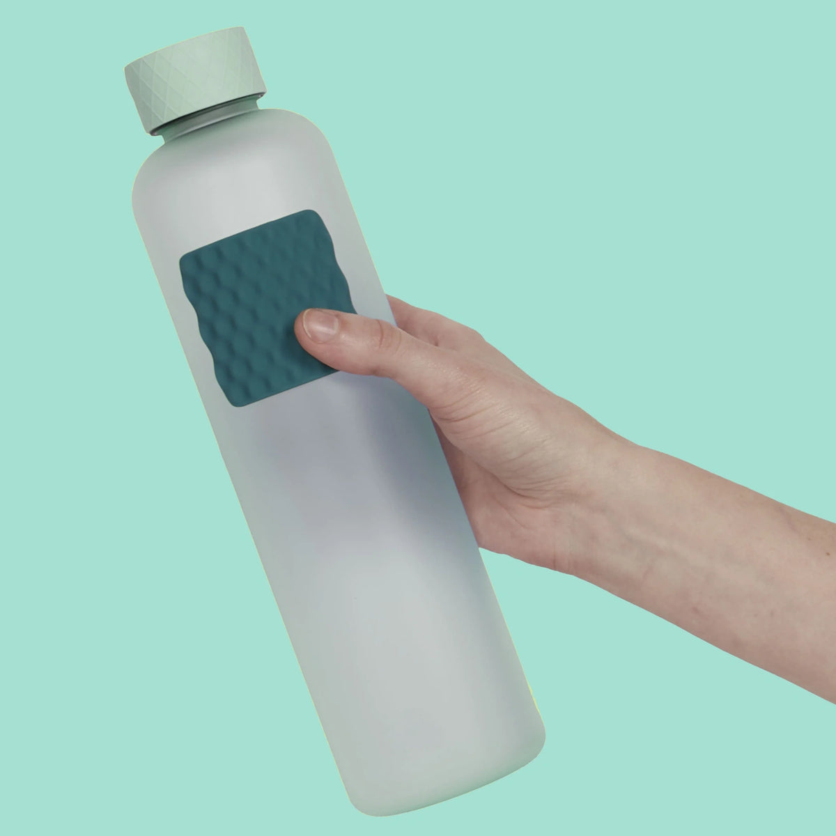 Hand holding a light blue water bottle with a dark green textured sensory sticker attached.