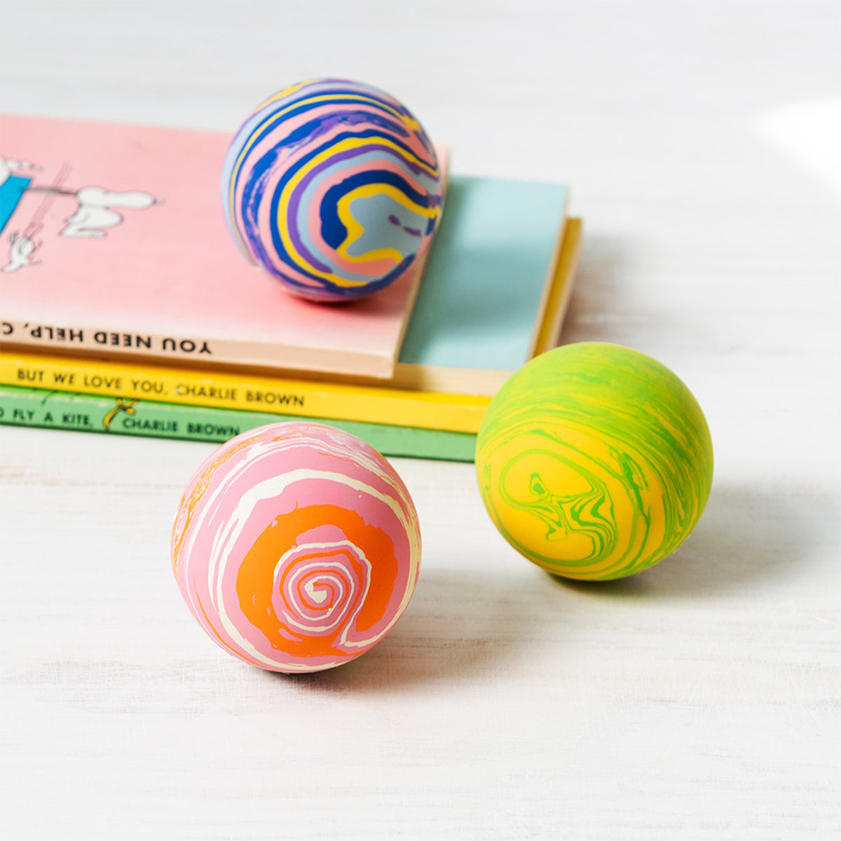 Three colorful, marbled bouncy balls rest on a white surface next to a small stack of children's books.