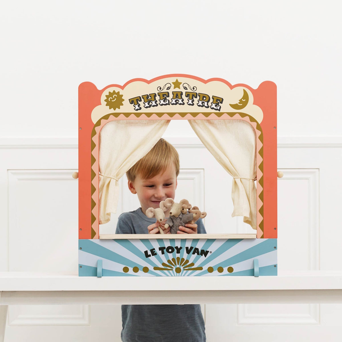 A young boy putting on a puppet show with small animal toys inside a wooden tabletop theater.