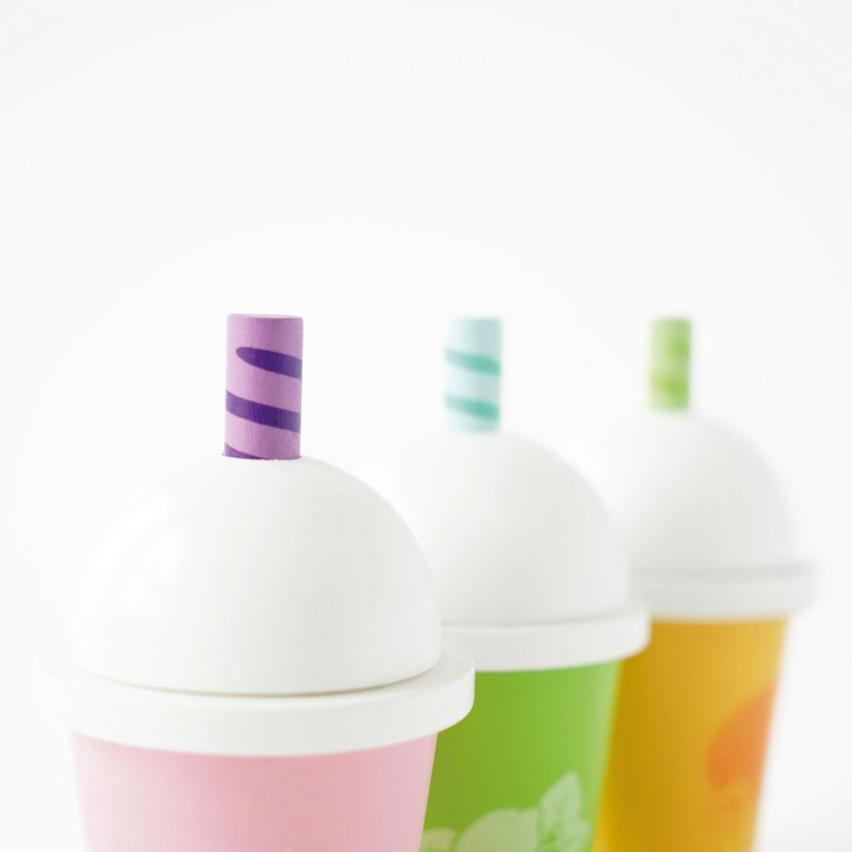Close-up of three wooden play smoothie cups with white domed lids and striped straws.
