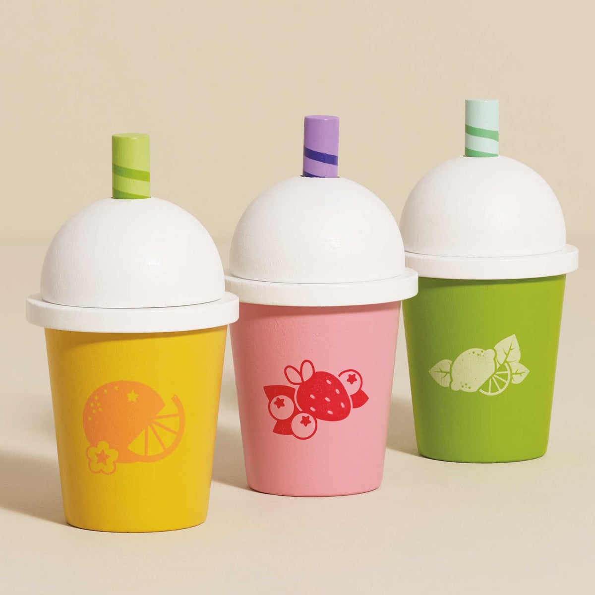 Three wooden play smoothie cups in yellow, pink, and green against a neutral beige background.