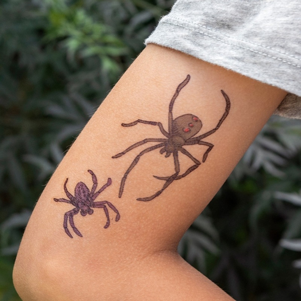 Close-up of a person's arm featuring two realistic temporary spider tattoos.