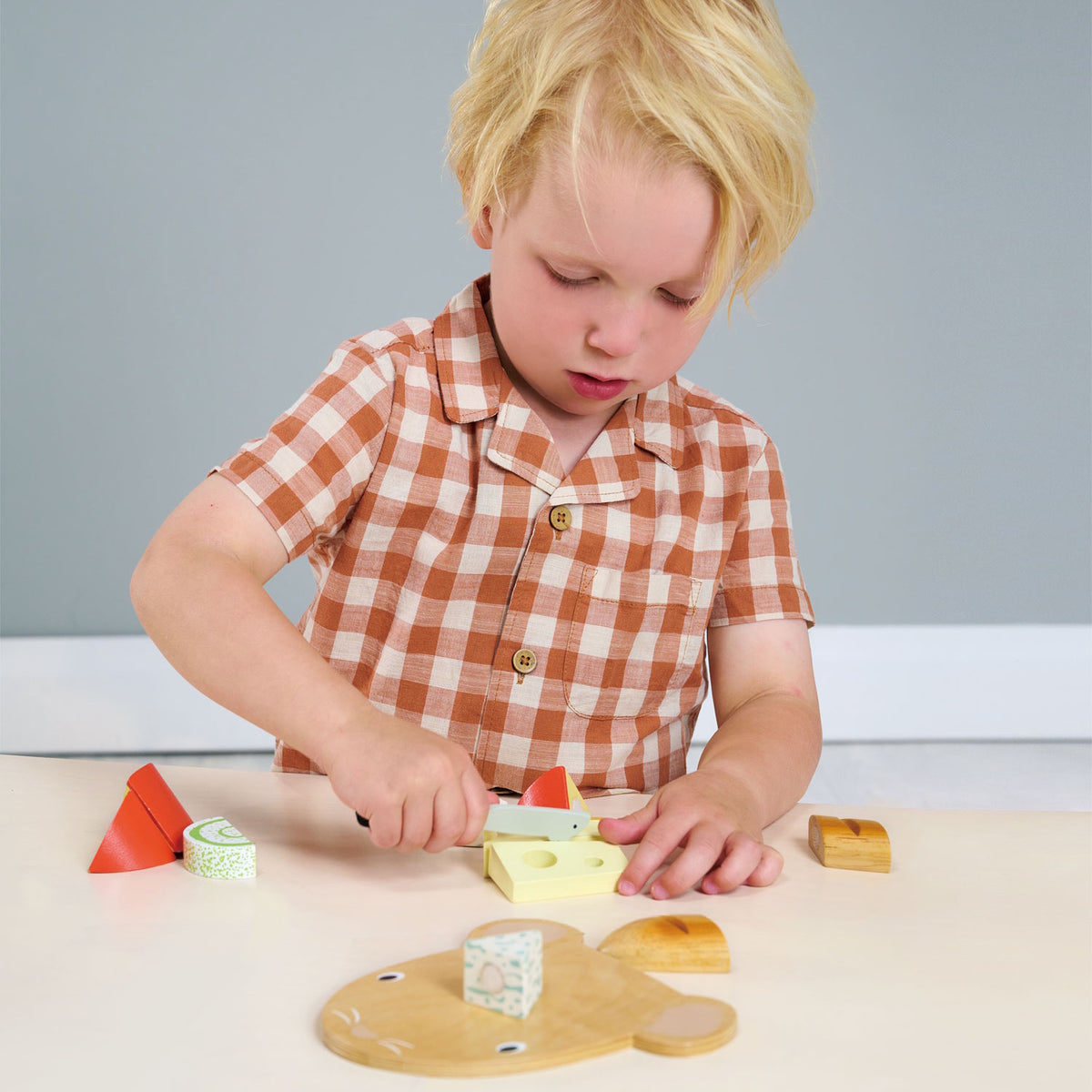 Child playing with a wooden cheese chopping board set and a toy knife.
