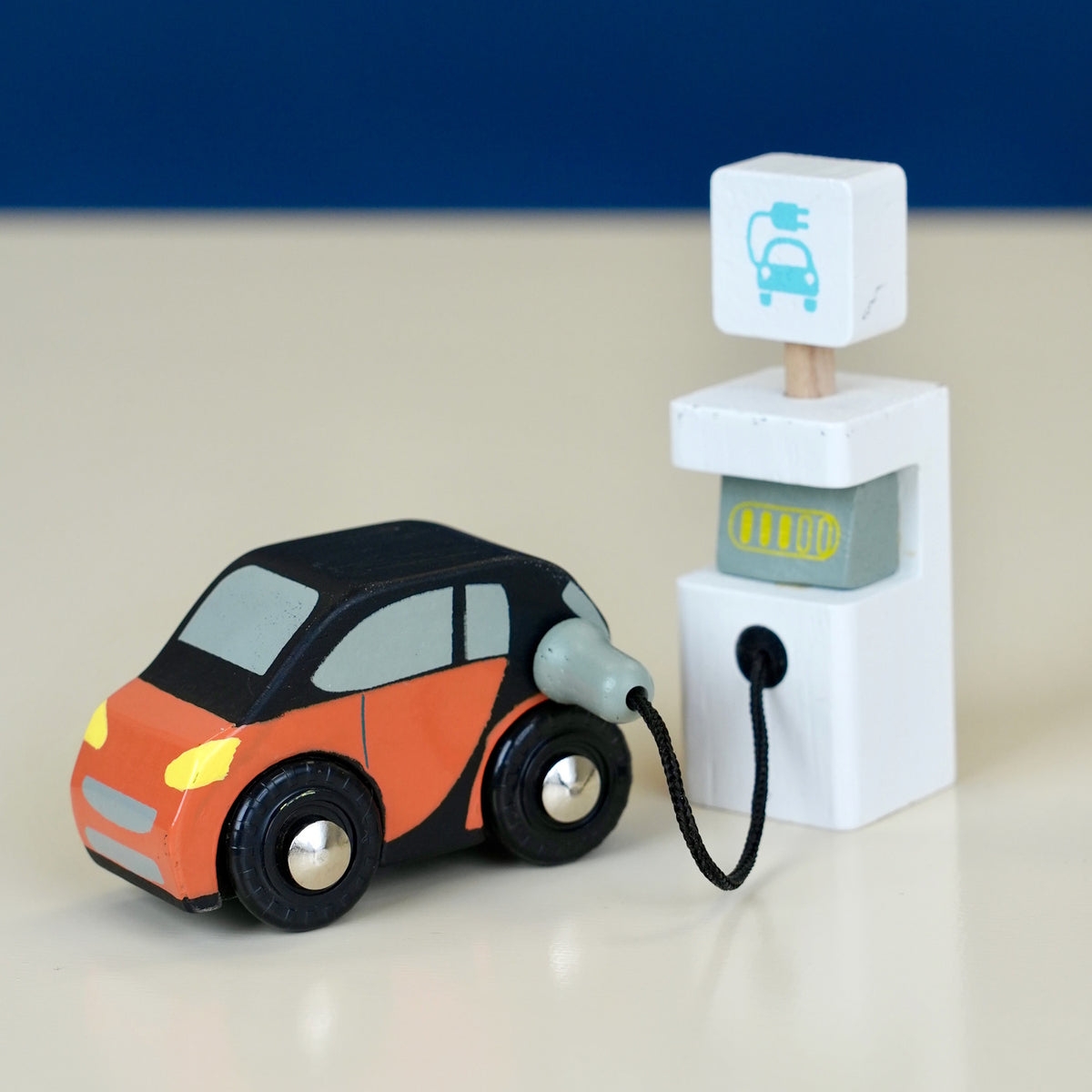 Orange toy car plugged into a white electric charging station.
