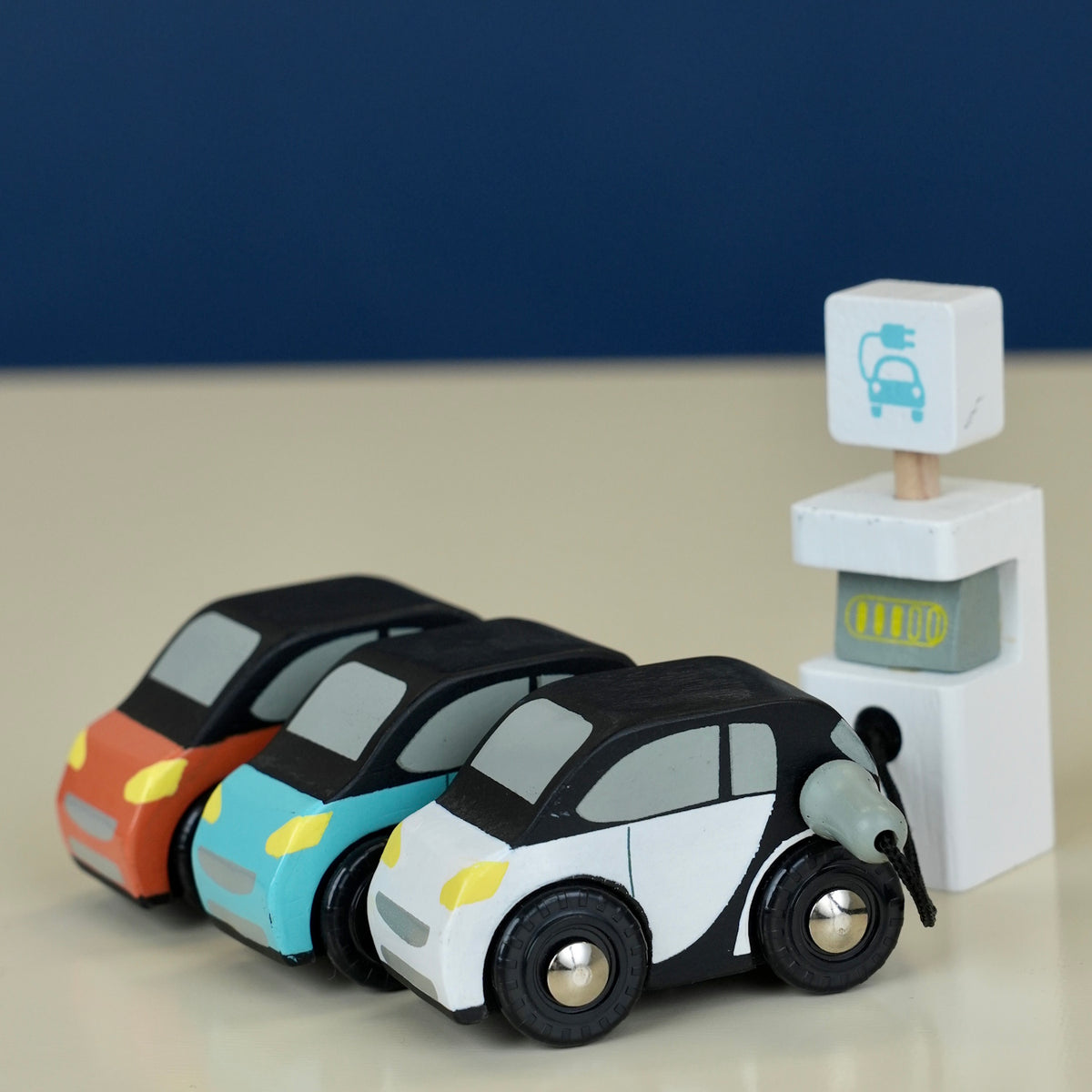 Three toy cars parked near an electric charging station.